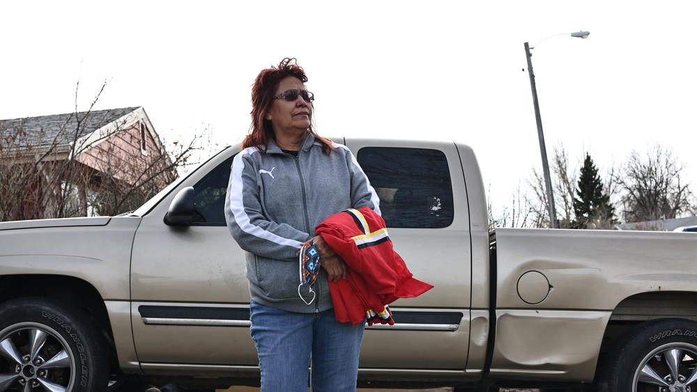 Jo Lynn Little Wounded holds her nephew Waylon's ribbon shirt beside his pickup truck.