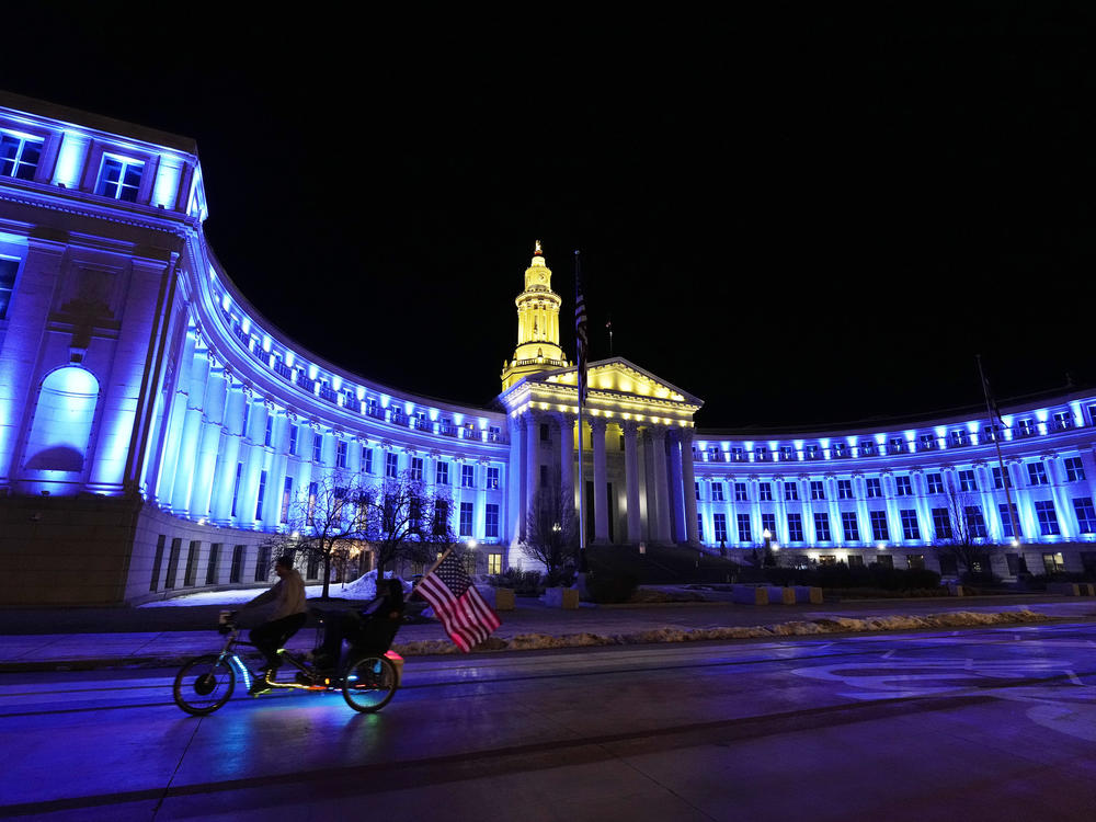 An American flag unfurls off a pedicab as it glides past the Denver City/County Building, which is illuminated in yellow and blue in support of Ukraine on Monday. Colorado's State Capitol will also be illuminated in blue and yellow in support of Ukraine.