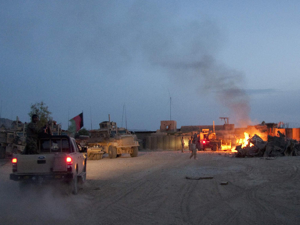 In this April 28, 2011, photo, an Afghan national army pickup truck passes parked U.S. armored military vehicles as smoke rises from a fire in a trash burn pit at Forward Operating Base Caferetta Nawzad, Helmand province south of Kabul, Afghanistan.