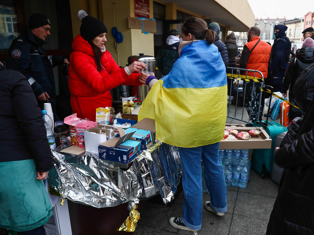 A woman wearing the Ukrainian flag is handed a beverage at the train station in Przemysl, Poland,  on Thursday. Ukrainians have been welcomed into Poland and other neighboring countries as they flee Russian attacks.