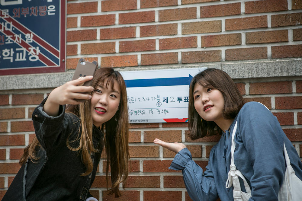 Young South Koreans take a snapshot at the entrance of a polling site after casting a vote in the presidential election on May 9, 2017, in Seoul. In the 2022 election, candidates have been trying to win over voters in their 20s and 30s.