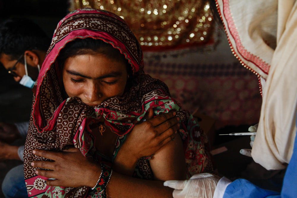 A young woman clenches her<em> dupatta</em>, or scarf, between her teeth as Namra, a 21-year-old health worker, injects her with a COVID-19 vaccine.