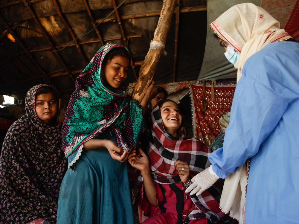 Young women wait to get vaccinated by Namra, a 21-year-old health worker who's part of a national door-to-door vaccination effort in the informal Hindubasti settlement in Karachi.