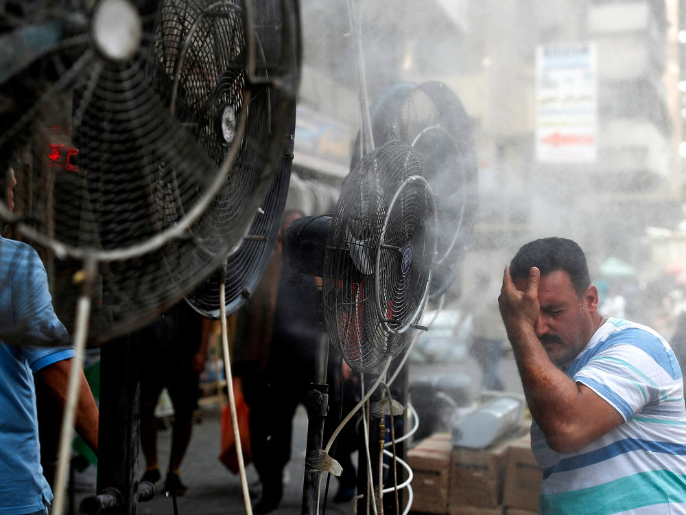 Fans spray air mixed with water vapor to cool down pedestrians on a Baghdad street on June 30, 2021, during a heat wave.