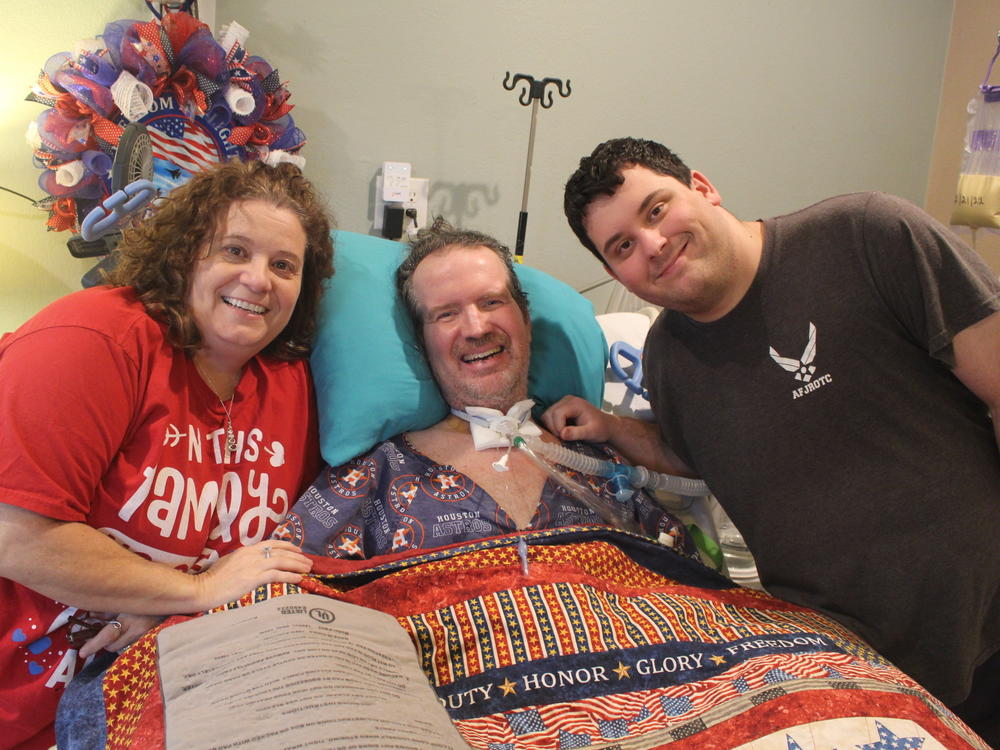 Lara and Trey Garey stand at the bedside of Tom Garey, an Air Force veteran with advanced ALS. Trey, 19, has spent much of his teenage years caring for his father at their Texas home.