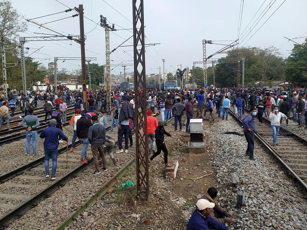 People gather near a train set on fire by a mob in Gaya protesting the restrictive qualifications set for railway jobs.