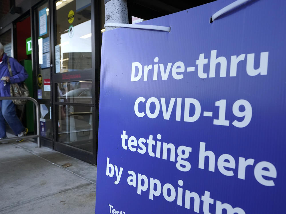 A passer-by walks past a sign that calls attention to COVID-19 testing while departing a Walgreens pharmacy, Wednesday, Dec. 15, 2021, in New Bedford, Mass. (AP Photo/Steven Senne)