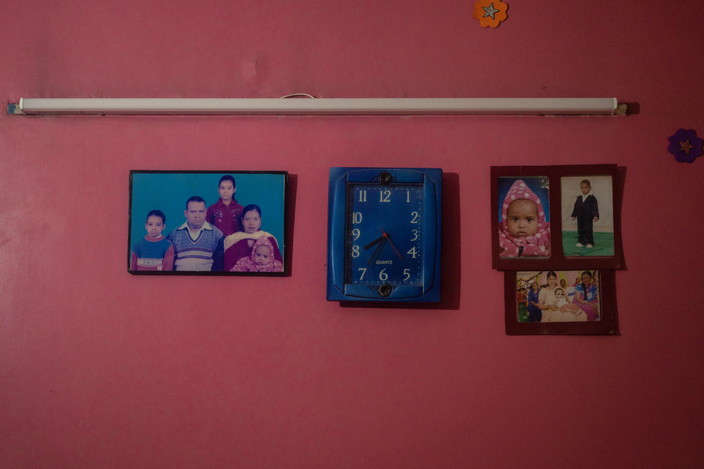<em>Pictures of Anand Singh, who died of COVID at age 50, with his wife, Radha Devi, and their three children are displayed on a wall in their living room in their modest home.</em>