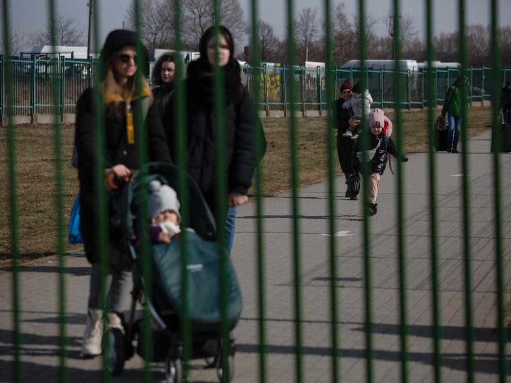 Refugees walk toward a green steel fence that marks the end of a buffer zone between Ukraine and Medyka, Poland.