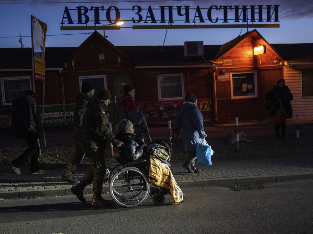 A Polish soldier helps a refugee who fled the war from Ukraine at the Medyka border crossing in Poland, on Saturday, March 12, 2022. Russian troops are pressing their offensive across Ukraine, pounding populated areas with artillery and airstrikes and deploying siege tactics honed in Syria and Chechnya — where opposing cities were reduced to rubble.
