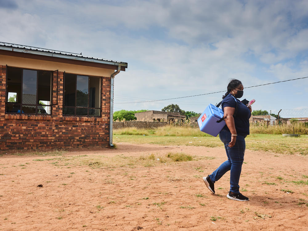A health worker carries a vaccine cooler during a rural vaccination drive in Mpumalanga, South Africa. A lot more money is needed for the steps required to get shots into people's arms: storage, transportation, health workers, campaigns to counter misinformation.