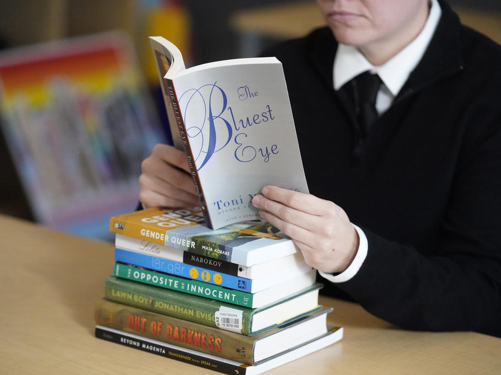 Amanda Darrow, director of youth, family and education programs at the Utah Pride Center, poses with books, including <em>The Bluest Eye</em>, by Toni Morrison and<em> Lawn Boy</em> by Jonathan Evison, that have been the subject of complaints from parents in Salt Lake City on Dec. 16, 2021.