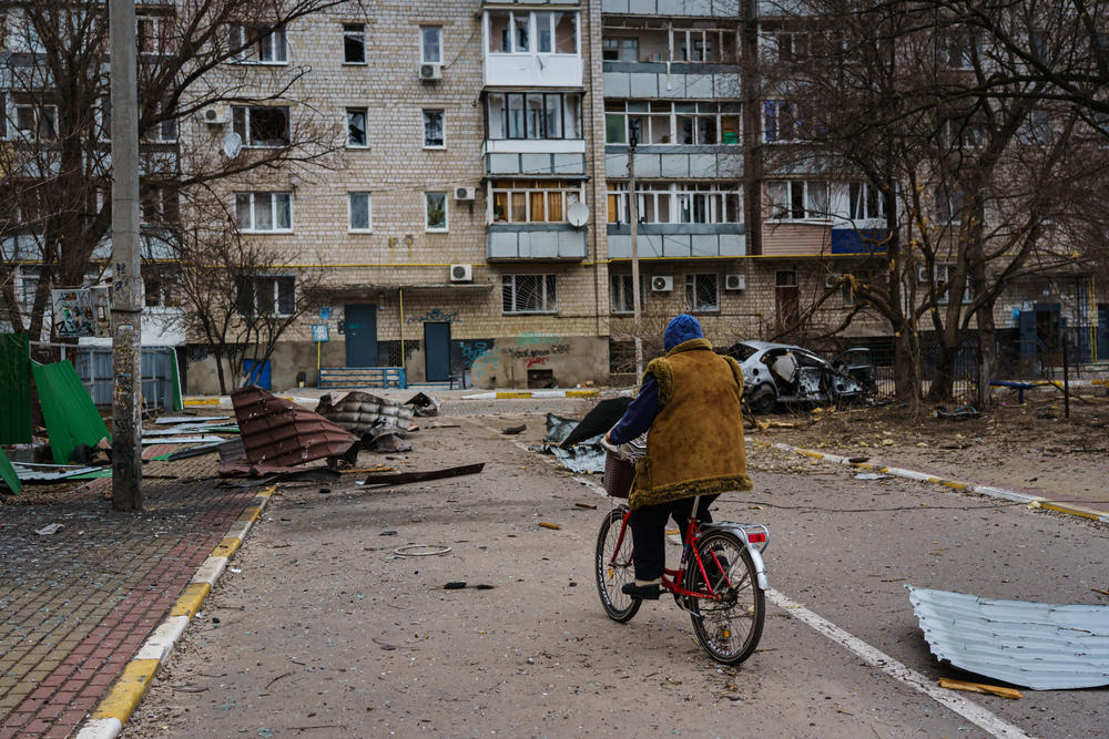 A woman bicycles past debris in a neighborhood that was bombarded by Russian forces in Irpin, Ukraine, Sunday, March 13, 2022.