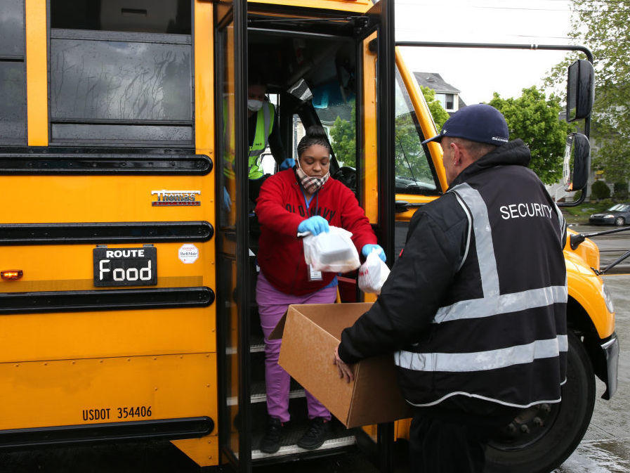 Nutritionist Shaunté Fields (center) and bus driver Treva White (behind Fields, on the bus) deliver meals to children and their families in Seattle. When schools closed because of COVID-19, Seattle Public Schools began distributing breakfast and lunch to students through a network of 26 school sites and 43 bus routes five days a week.