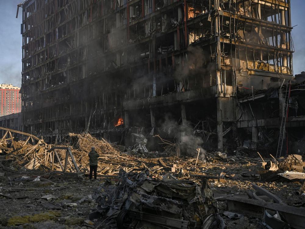 A man stands looking at the burning and destroyed Retroville shopping mall after a Russian attack on the northwest of the Ukrainian capital, Kyiv, on Monday. The high-rise building was hit by a powerful blast that also destroyed vehicles and left a large crater.