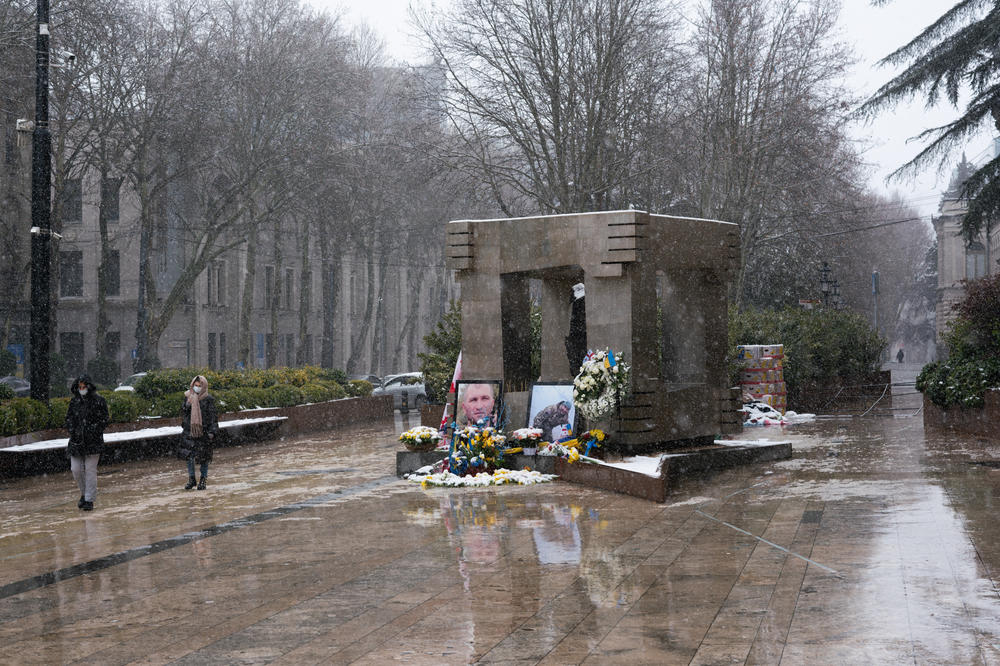 A memorial to Georgians who volunteered as soldiers and died in Ukraine sits outside Georgia's parliament building. The memorial of photos and flowers leans up against a permanent memorial for people who were killed in 1989 during an anti-Soviet protest that was crushed by the Soviet army.