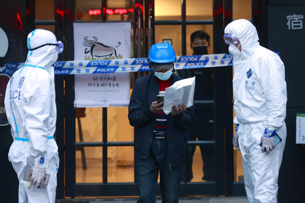 A delivery man walks by police officers with protective suit outside of a hotel in Shanghai, China, on March 15.