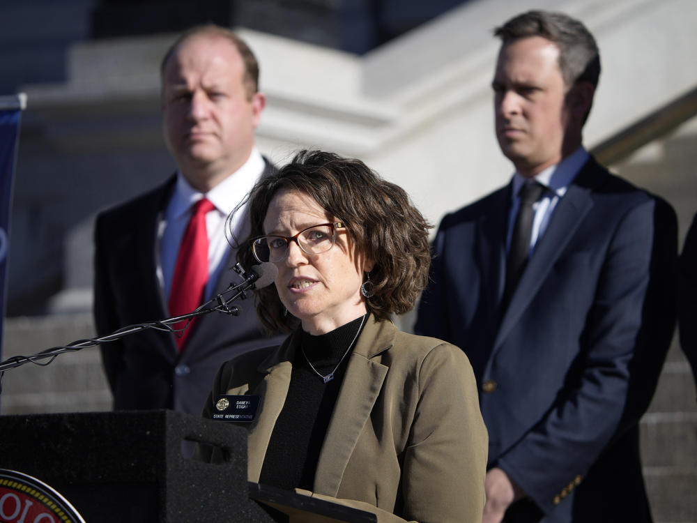 Colorado Governor Jared Polis, back left, and Colorado Senate Majority Leader Steve Fenberg, back right, listen as Majority Leader Daneya Esgar speaks during a news conference. Esgar has called for the U.S. Supreme Court to uphold <em>Roe v. Wade</em>.