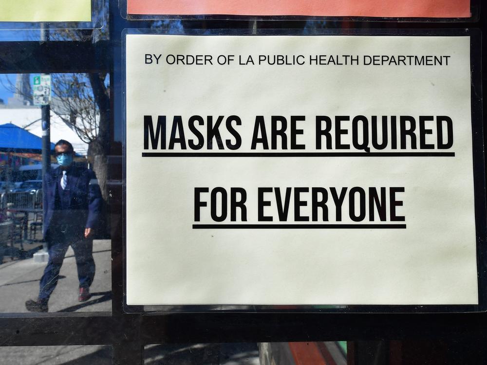 A man wearing a face mask walks past a sign requiring masks in Los Angeles on March 2. California dropped its mask requirements last month.