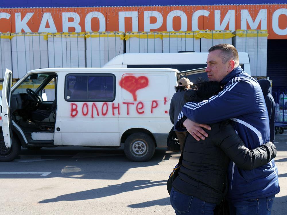 Olga and Oleksandr hug as they wait beside a vehicle painted with the word 