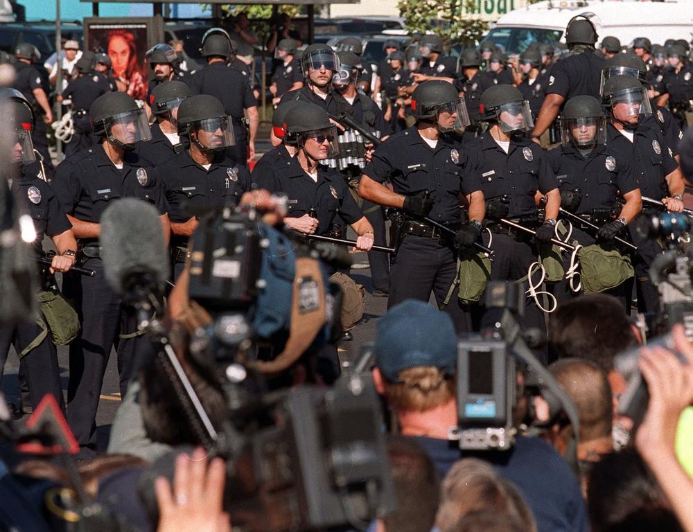 TV cameras film Los Angeles Police Department officers as they take over a street corner adjacent to the Staples Center, site of the 2000 Democratic National Convention, after a confrontation between police and protesters on Aug. 16, 2000.