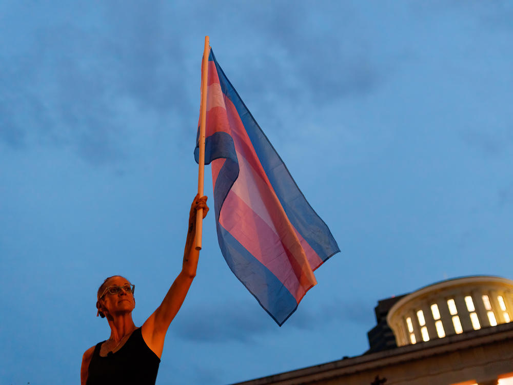 Cole Ramsey, 39, of South Linden, Ohio, holds a Transgender Pride Flag in front of the Ohio Statehouse in Columbus to protest the passing of legislation against trans women playing sports in high school and college.