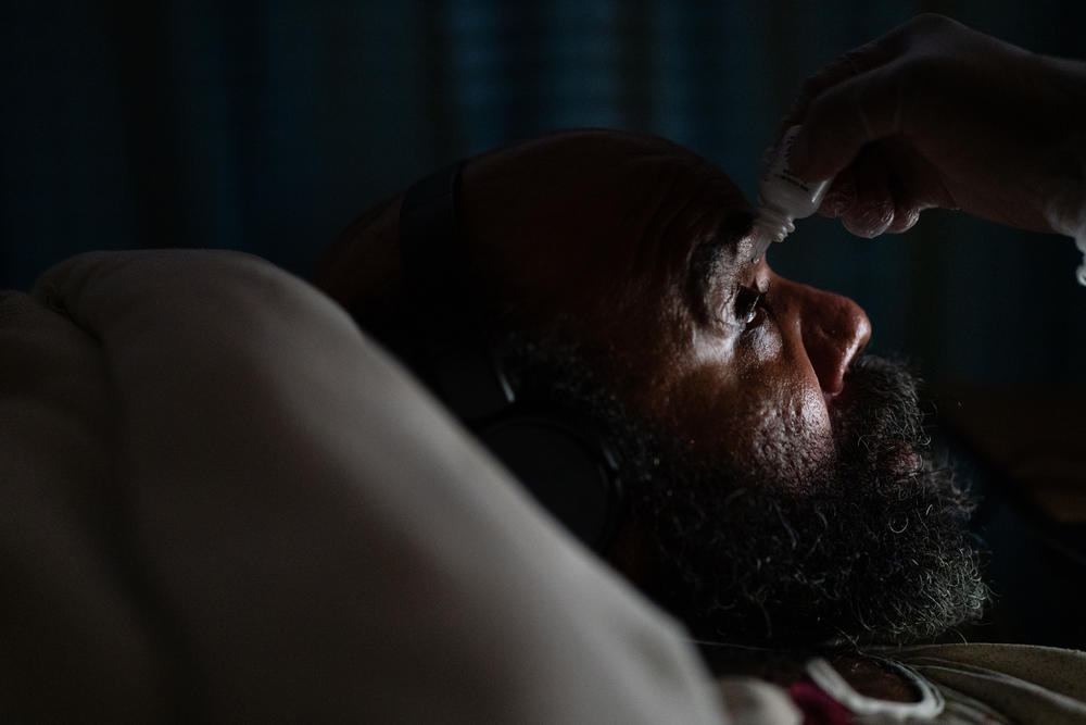 A staff member wearing protective gloves administers eye drop medication to Maurice Miller in his room at the nursing home.