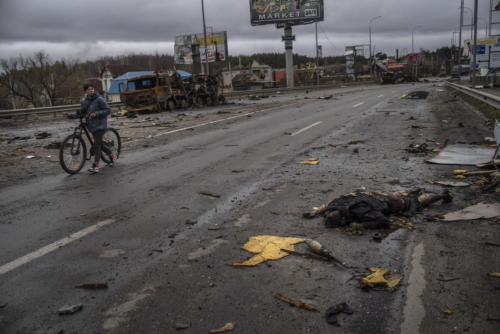 <strong>April 2:</strong> A woman walks next to a dead Russian soldier in Bucha, on the outskirts of Kyiv. As Russian forces pull back from Ukraine's capital region, retreating troops are creating a 