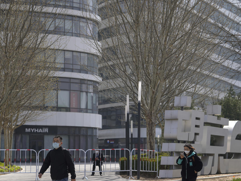 Residents wearing face masks walk by a masked security watch over a barricaded Galaxy Soho commercial office building locked down for health monitoring following a COVID-19 case detected in the area Tuesday in Beijing. China has sent more than 10,000 health workers from across the country to Shanghai, including 2,000 military medical staff.