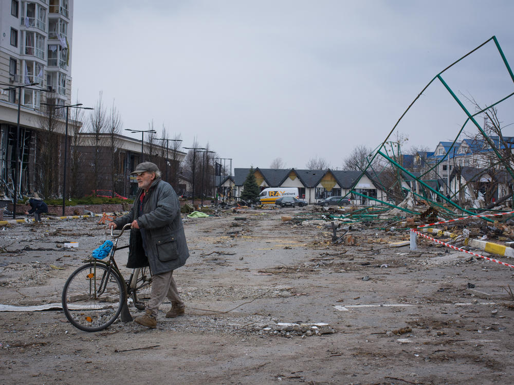 A man walks his bike through a parking lot littered with broken glass in Bucha, Ukraine.