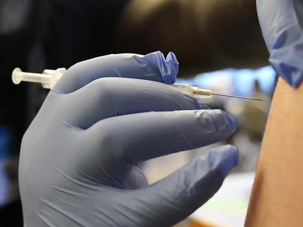 DeMarcus Hicks, a recent graduate of nursing school who is working as a contractor with the Federal Emergency Management Agency, gives a person a Pfizer COVID-19 vaccine booster shot, Dec. 20, 2021, in Federal Way, Wash.