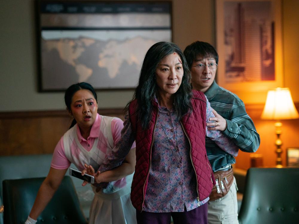 Michelle Yeoh (center) plays Evelyn Wang, a Chinese immigrant who owns a failing laundromat. She protects her daughter Joy (left), played by Stephanie Hsu, and her husband Waymond (right), played by Ke Huy Quan.