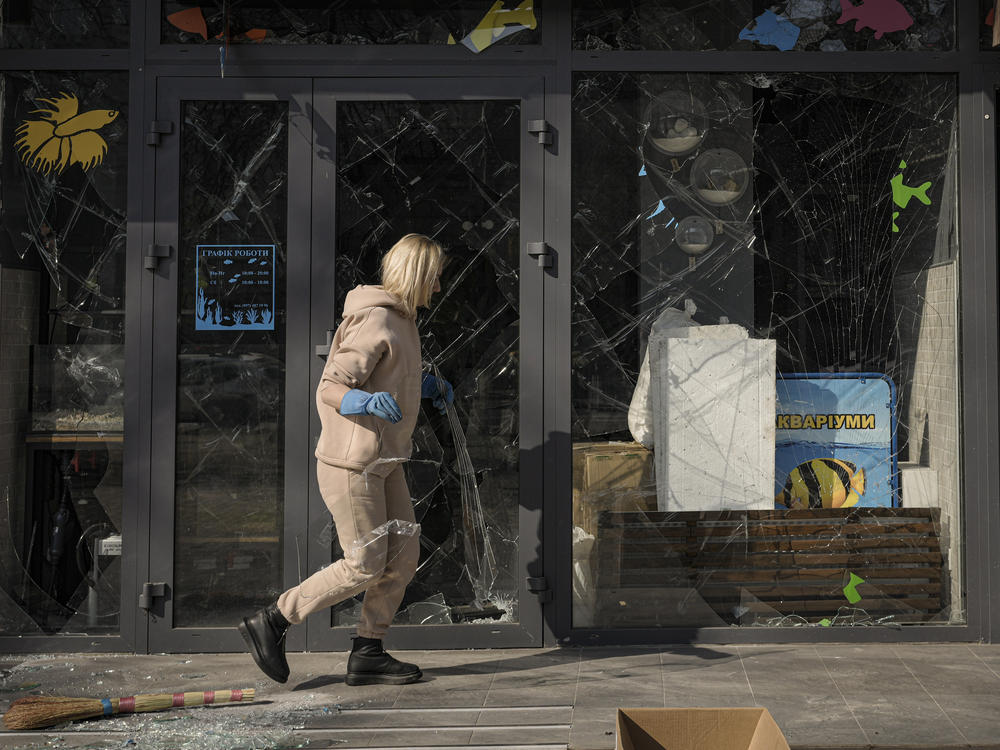 A woman removes pieces of broken glass from a shop window after a bombing in Kyiv, Ukraine, on March 23.