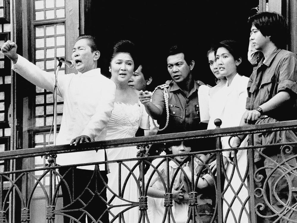 Ferdinand Marcos, with his wife Imelda at his side and Ferdinand Marcos Jr., far right, gestures from the balcony of Malacanang Palace on Feb. 25, 1986, in Manila, after taking the oath of office as president of the Philippines. The family fled to the U.S. shortly thereafter.