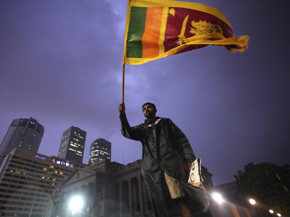 A man waves a Sri Lankan national flag as he stands on a barricade blocking the entrance to president's office during a protest in Colombo, Sri Lanka on Monday.