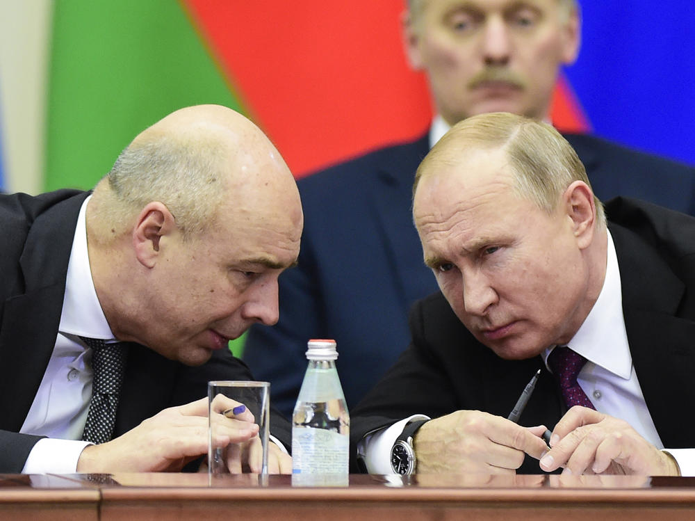 Russia's Finance Ministry is threatening to sue, saying economic sanctions from the U.S. and its allies are preventing the country from making interest payments in dollars to foreign investors. Here, Russian President Vladimir Putin (right) and Finance Minister Anton Siluanov chat during a meeting in 2018.