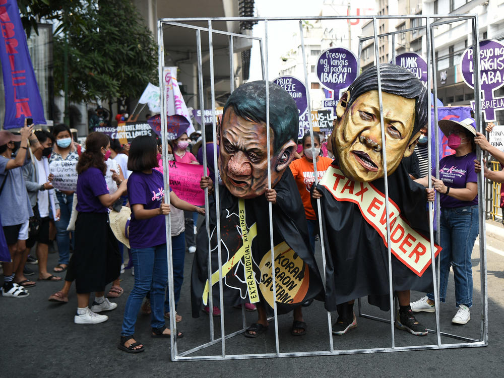 Women activists hold a makeshift prison cell with colleagues wearing masks depicting President Rodrigo Duterte (left) and Ferdinand 
