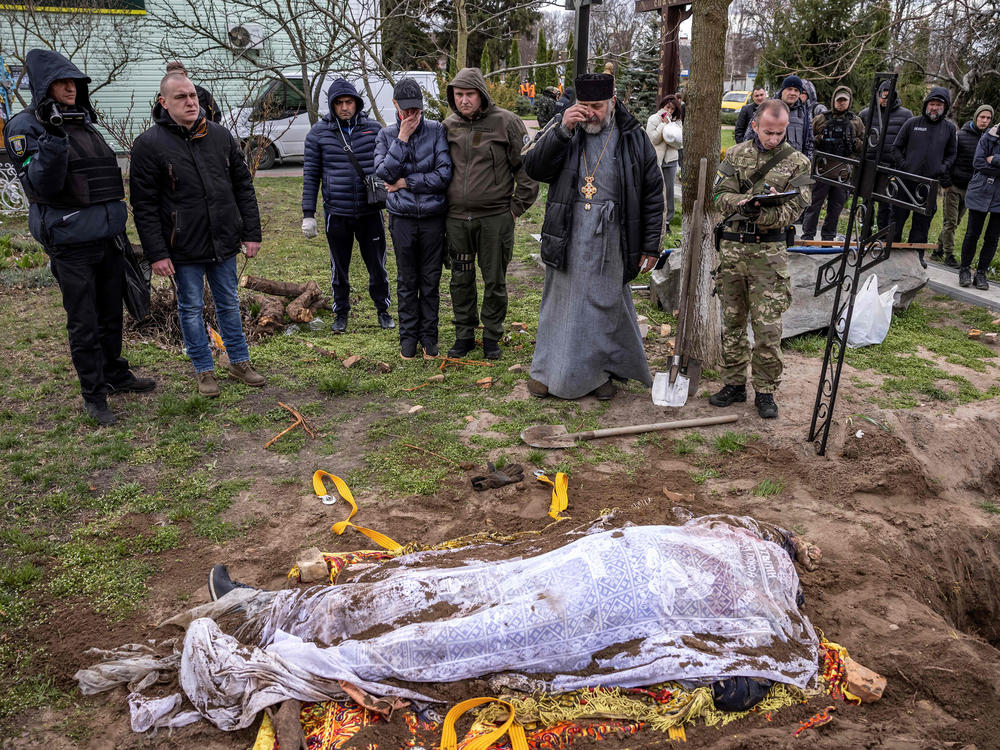 A priest and relatives on Tuesday stand near the exhumed body of Gostomel's mayor, Yuriy Prylypko, who had been buried near a church in the village in the Kyiv region. Prylypko, 62, was killed on March 7 after Russian forces rolled into his village.