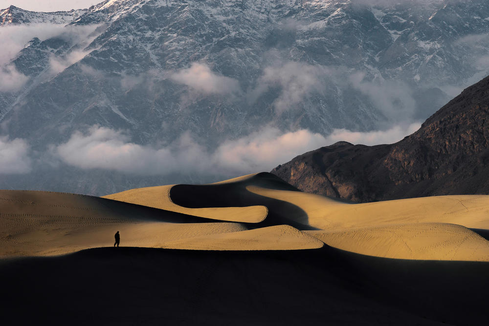 A man walks along a sand dune in the cold desert as a mountain looms in Skardu, Pakistan.