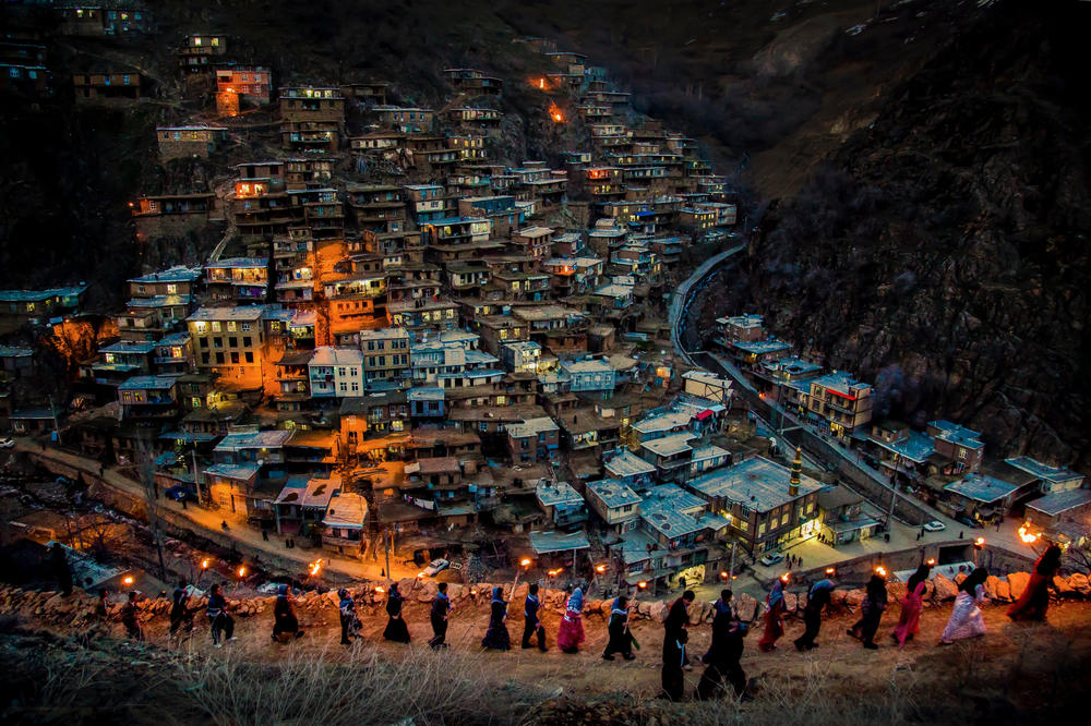 A line of men and women with torches walk along a ridge above a city nestled in the mountainside in Kurdistan.<strong> </strong>