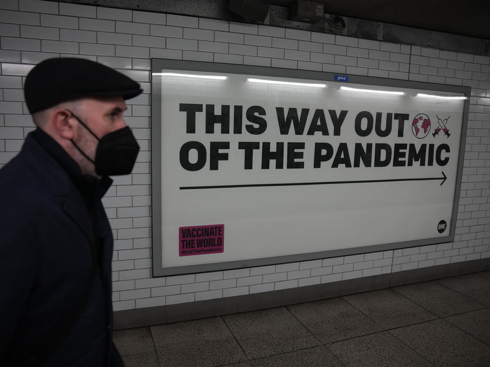 A man wearing a face mask to curb the spread of coronavirus walks past a health campaign poster in the Westminster underground train station, in London.