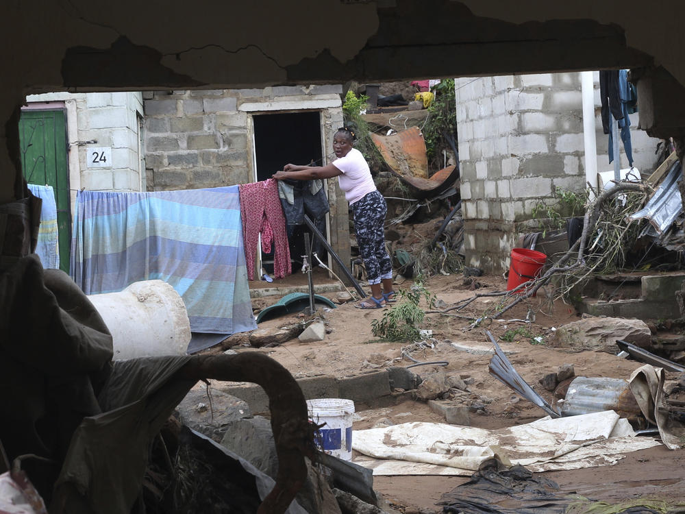 A woman is seen through a damaged wall hanging her clothes on a makeshift washing line in Ntuzuma, outside of Durban, South Africa, on Wednesday. Flooding in South Africa's Durban area has taken killed at least 259.