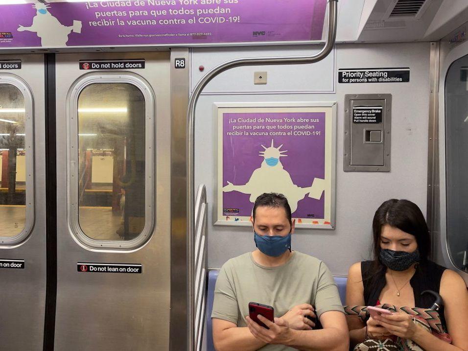 Travelers wearing masks sit in the subway where posters advertise free COVID-19 vaccination in New York City in several languages on July 18, 2021.
