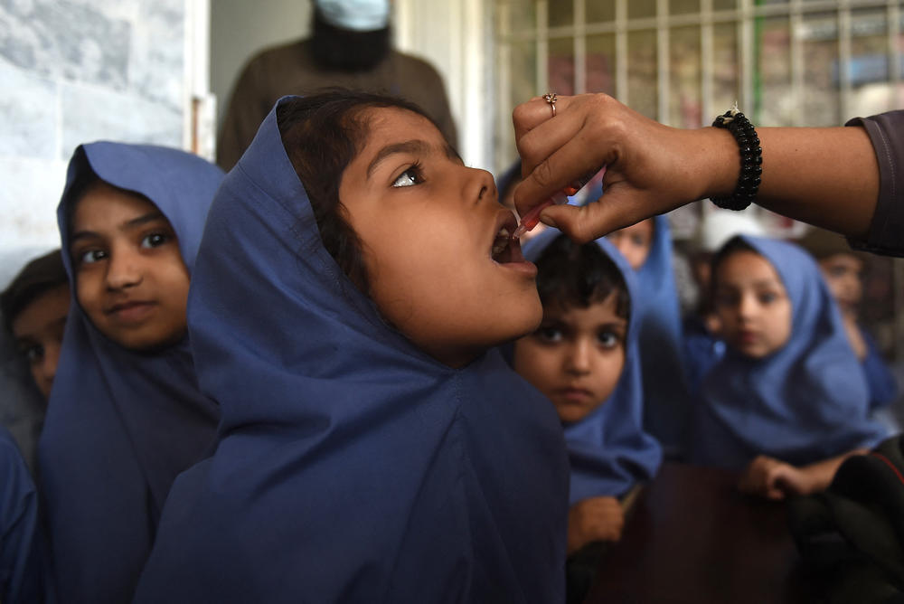 A health worker administers the oral polio vaccine to a young girl as other children wait for their turn at a school in Karachi, Pakistan on February 28, 2022. In response to an uptick in cases of vaccine-derived polio — a form of the disease that stems from the oral vaccine — many countries are rolling out a new oral polio vaccine.