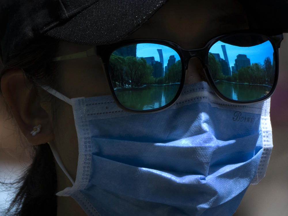 The skyline of Beijing is reflecting in the sunglasses of a woman wearing a face mask as she walks at a public park in Beijing, Thursday, April 14, 2022.