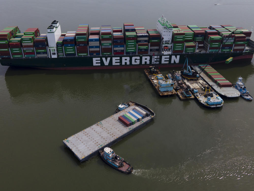 Tugboats, bottom, align a barge near the container ship Ever Forward, top, which ran aground last month, as workers remove containers from it in efforts to lighten the load and refloat the vessel on  April 13.