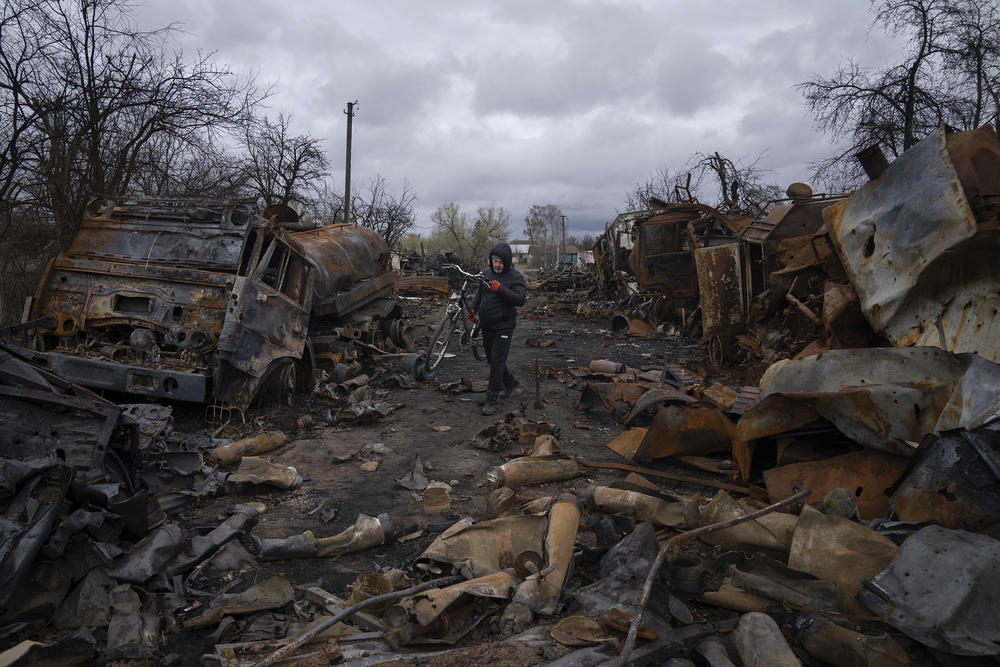 <strong>April 17:</strong> A man carries a bicycle down a street littered with ruined Russian military vehicles near Chernihiv, Ukraine.