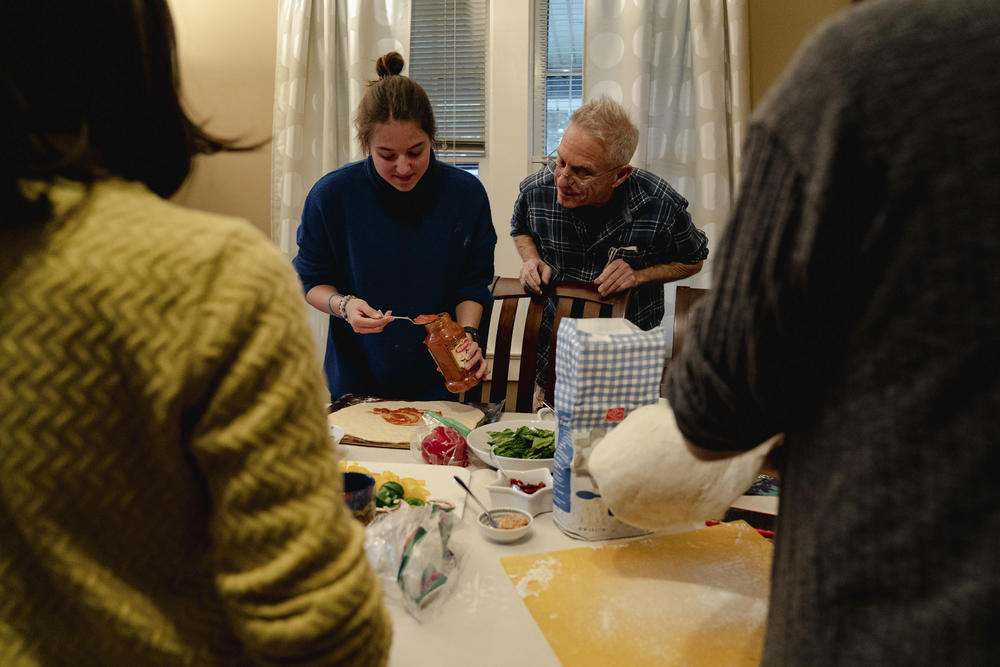David Gaines guides Erika as she puts tomato sauce onto pizza dough.