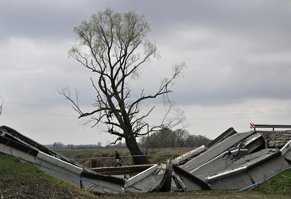 <strong>April 16:</strong> A man crosses a river next to a ruined bridge in the village of Rusaniv, in the Kyiv Oblast.