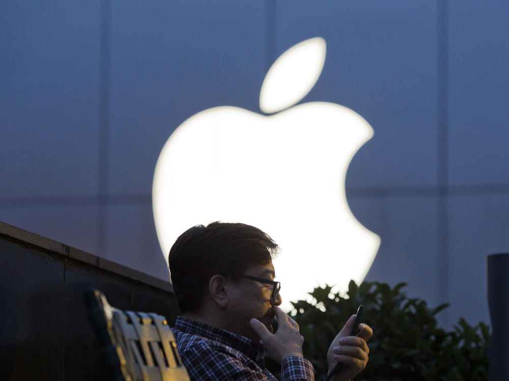 A man uses his mobile phone near an Apple store logo in Beijing.
